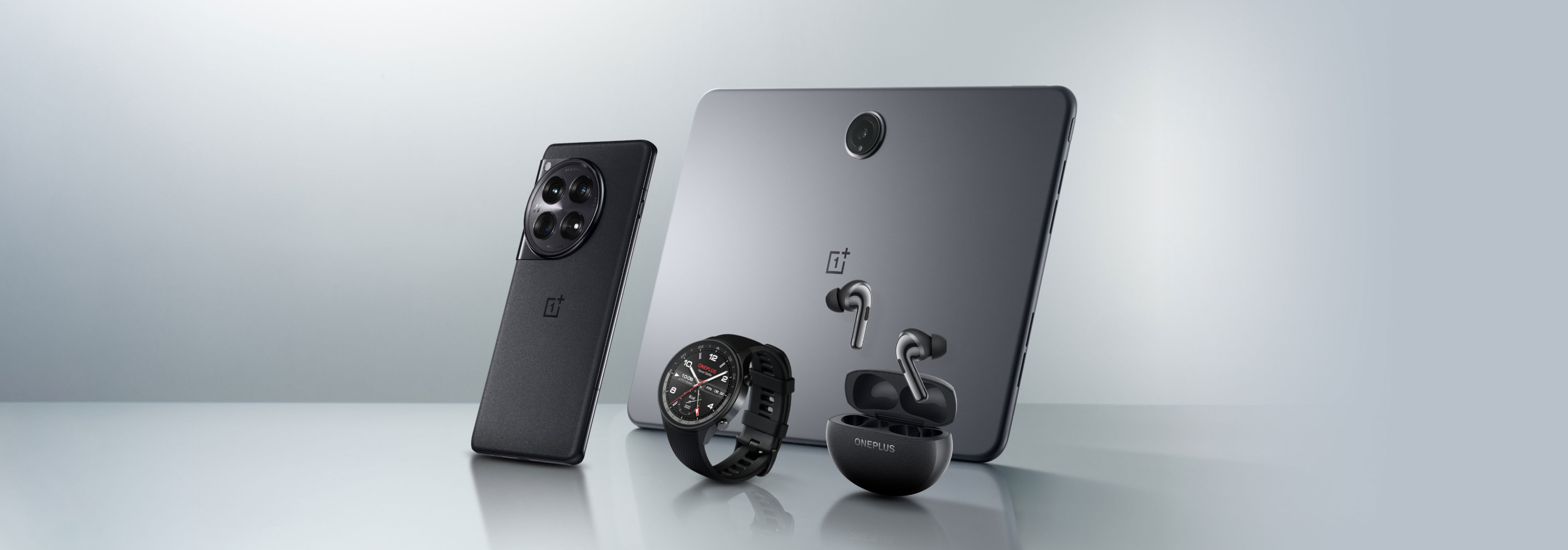 Gray and black colored mobile devices, watches, and wireless earbuds on a reflective surface.
